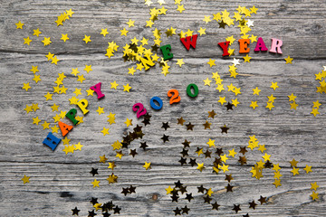 2020 Happy New year text for greeting card, with gold stars and colored letters on wooden background, calendar, invitation