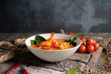 Tom Yam soup with shrimp, squid and hot pepper on textured wooden board.The concept of national cuisine