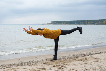 Woman practicing yoga against the blue sky and the azure sea on the sandy shore.