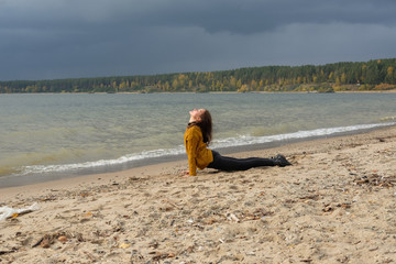 Woman practicing yoga against the blue sky and the azure sea on the sandy shore.