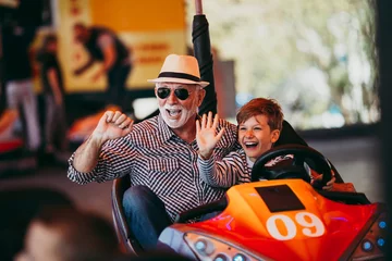Foto op Plexiglas Amusementspark Grootvader en kleinzoon hebben plezier en brengen goede quality time samen door in het pretpark. Ze genieten en glimlachen terwijl ze samen in een botsauto rijden.
