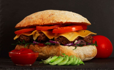 Closeup of delicious fresh homemade burger with lettuce, cheese, onions and tomatoes on dark background