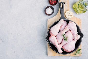 Raw uncooked chicken legs with rosemary and spices in cast iron pan.