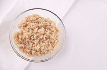 Cooked delicious quinoa in glass bowl with white napkin on the white table. Top view.