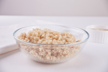 Cooked delicious quinoa in glass bowl with white napkin on the white table