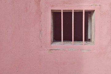 Fototapeta na wymiar Basement window with grate on the old pink wall