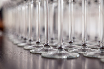 Many transparent crystal wine glasses stand in row on the brown wooden shelves of the rack. Side view. Concept of tasting, banquet, catering, buffet, lunch, anniversary, wedding, birthday