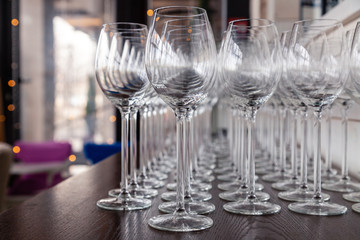 Many transparent crystal wine glasses stand in row on the brown wooden shelves of the rack. Side view. Concept of tasting, banquet, catering, buffet, lunch, anniversary, wedding, birthday