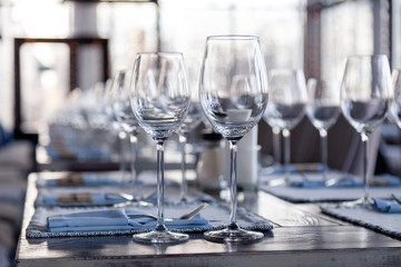 Restaurant interior, modern setting, wine and water glasses, forks and knives on textile napkins stand in row on vintage wooden table. Concept banquet, birthday, conference, group lunch