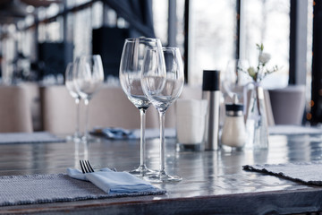 Restaurant interior, modern setting, wine and water glasses, forks and knives on textile napkins stand in row on vintage wooden table. Concept banquet, birthday, conference, group lunch