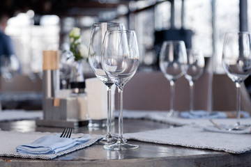 Restaurant interior, modern setting, wine and water glasses, forks and knives on textile napkins stand in row on vintage wooden table. Concept banquet, birthday, conference, group lunch