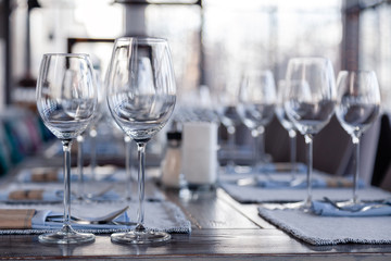 Restaurant interior, modern setting, wine and water glasses, forks and knives on textile napkins stand in row on vintage wooden table. Concept banquet, birthday, conference, group lunch