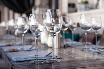 Restaurant interior, modern setting, wine and water glasses, forks and knives on textile napkins stand in row on vintage wooden table. Concept banquet, birthday, conference, group lunch