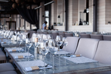 Restaurant interior, modern setting, wine and water glasses, forks and knives on textile napkins stand in row on vintage wooden table. Concept banquet, birthday, conference, group lunch