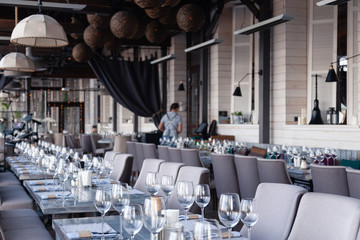 Restaurant interior, modern setting, wine and water glasses, forks and knives on textile napkins stand in row on vintage wooden table. Concept banquet, birthday, conference, group lunch
