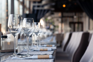 Restaurant interior, modern setting, wine and water glasses, forks and knives on textile napkins stand in row on vintage wooden table. Concept banquet, birthday, conference, group lunch