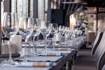 Restaurant interior, modern setting, wine and water glasses, forks and knives on textile napkins stand in row on vintage wooden table. Concept banquet, birthday, conference, group lunch