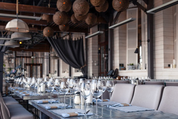 Restaurant interior, modern setting, wine and water glasses, forks and knives on textile napkins stand in row on vintage wooden table. Concept banquet, birthday, conference, group lunch