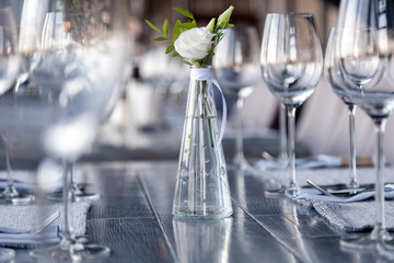 Modern restaurant setting, glass vase with bouquet flowers on table in restaurant. Wine and water glasses stand on wooden table. Concept banquet, birthday, conference, wedding