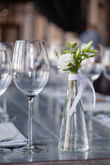 Modern restaurant setting, glass vase with bouquet flowers on table in restaurant. Wine and water glasses stand on wooden table. Concept banquet, birthday, conference, wedding