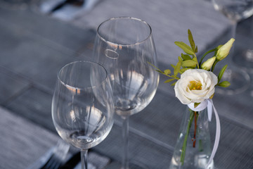 Modern restaurant setting, glass vase with bouquet flowers on table in restaurant. Wine and water glasses stand on wooden table. Concept banquet, birthday, conference, wedding