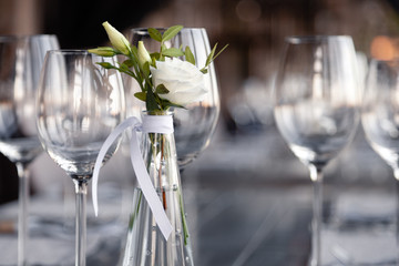 Modern restaurant setting, glass vase with bouquet flowers on table in restaurant. Wine and water glasses stand on wooden table. Concept banquet, birthday, conference, wedding