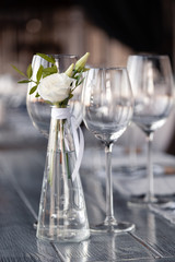 Modern restaurant setting, glass vase with bouquet flowers on table in restaurant. Wine and water glasses stand on wooden table. Concept banquet, birthday, conference, wedding