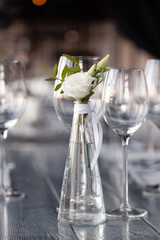 Modern restaurant setting, glass vase with bouquet flowers on table in restaurant. Wine and water glasses stand on wooden table. Concept banquet, birthday, conference, wedding