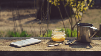 Metal mug, a jar of honey and a telephone on a wooden table
