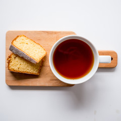 Cup of tea and two slices of sponge cake on a wooden chopping board. Top view. Squared format.