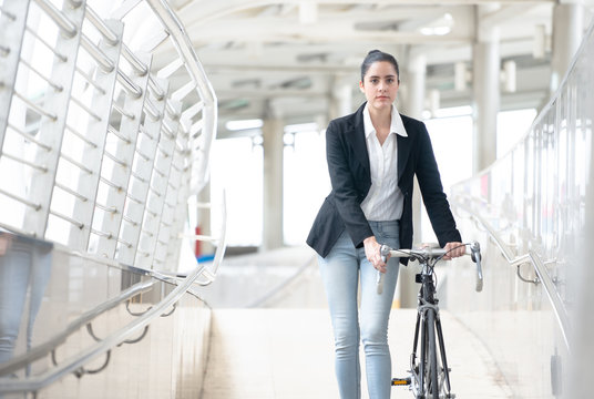Young business woman with bike walking along sidewalk outdoors in urban city, Pushing Bike City Concept.