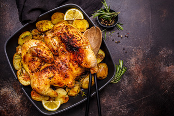 Roasted whole chicken with potatoes in a grill pan, copy space, dark background.