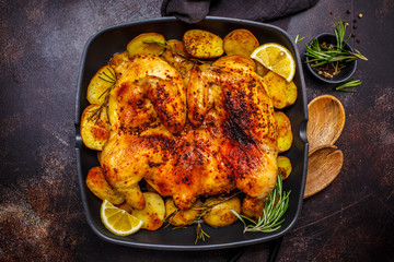 Roasted whole chicken with potatoes in a grill pan, dark background.