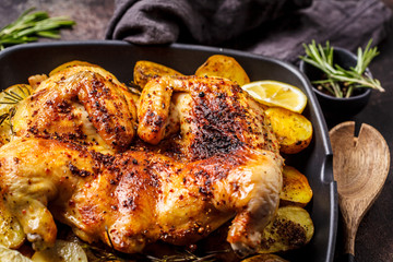 Roasted whole chicken with potatoes in a grill pan, dark background.