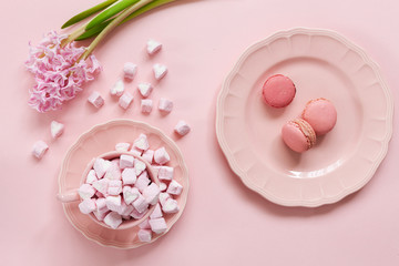 Pink marshmallow and pink macaroons in pink dishes and pink hyacinth on pink background