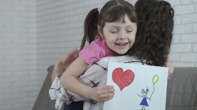 The child gives mom a drawing. Mother hugging her adorable daughter with a pattern.