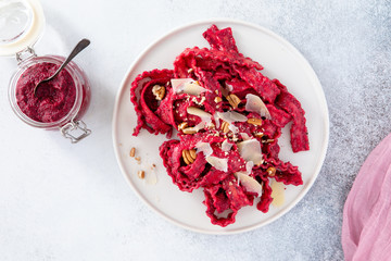 Top view of vegetarian mafaldine pasta with beet pesto sauce, walnut and parmesan cheese on a white background