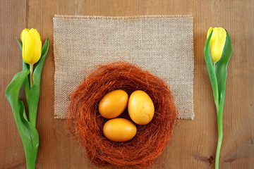 Jajka barwione kurkumą otoczone żółtymi tulipanami i brązowym sizalem - obrazy, fototapety, plakaty