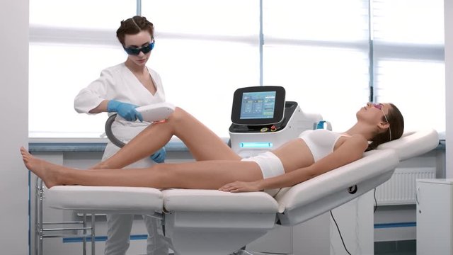 Beautician perform laser hair removal procedure on patient's leg