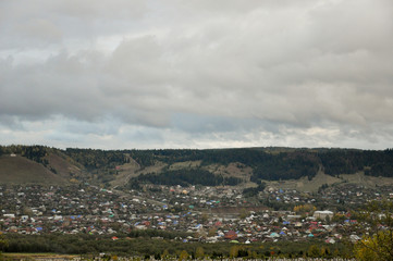 Heavy grey clouds in the cold autumn sky over  village with small houses far away in the mountains and fields. Travelling. People living