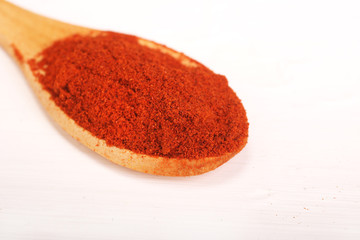 Wooden serving spoon full of red pepper paprika spice powder isolated over the white background