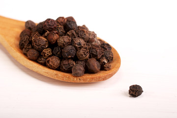 Wooden serving spoon full of black pepper spice isolated over the white background