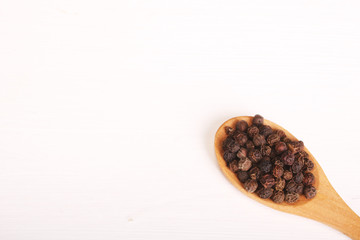 Wooden serving spoon full of black pepper spice isolated over the white background