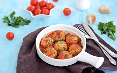 Fish meatballs in tomato sauce in a white ceramic pan on a light blue concrete background.