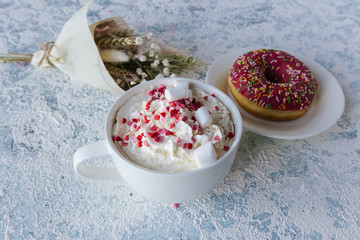 A cup of coffee with whipped cream and a berry pink donut