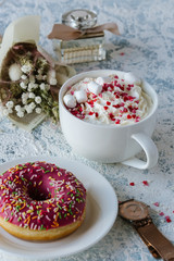 A cup of coffee with whipped cream and a berry pink donut
