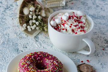 A cup of coffee with whipped cream and a berry pink donut