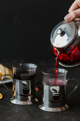 Waiter pours  fruit tea with oranges and berries in a teapot, two tea cups with cheesecakes