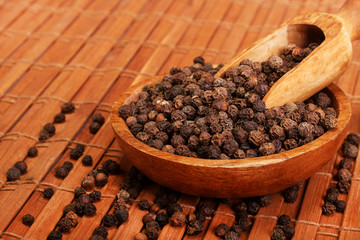 Wooden serving spoon shovel full of black pepper spice balls in wooden bowl isolated over the wooden background