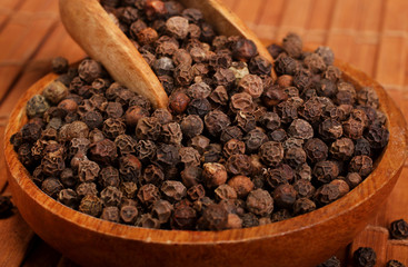Wooden serving spoon shovel full of black pepper spice balls in wooden bowl isolated over the wooden background